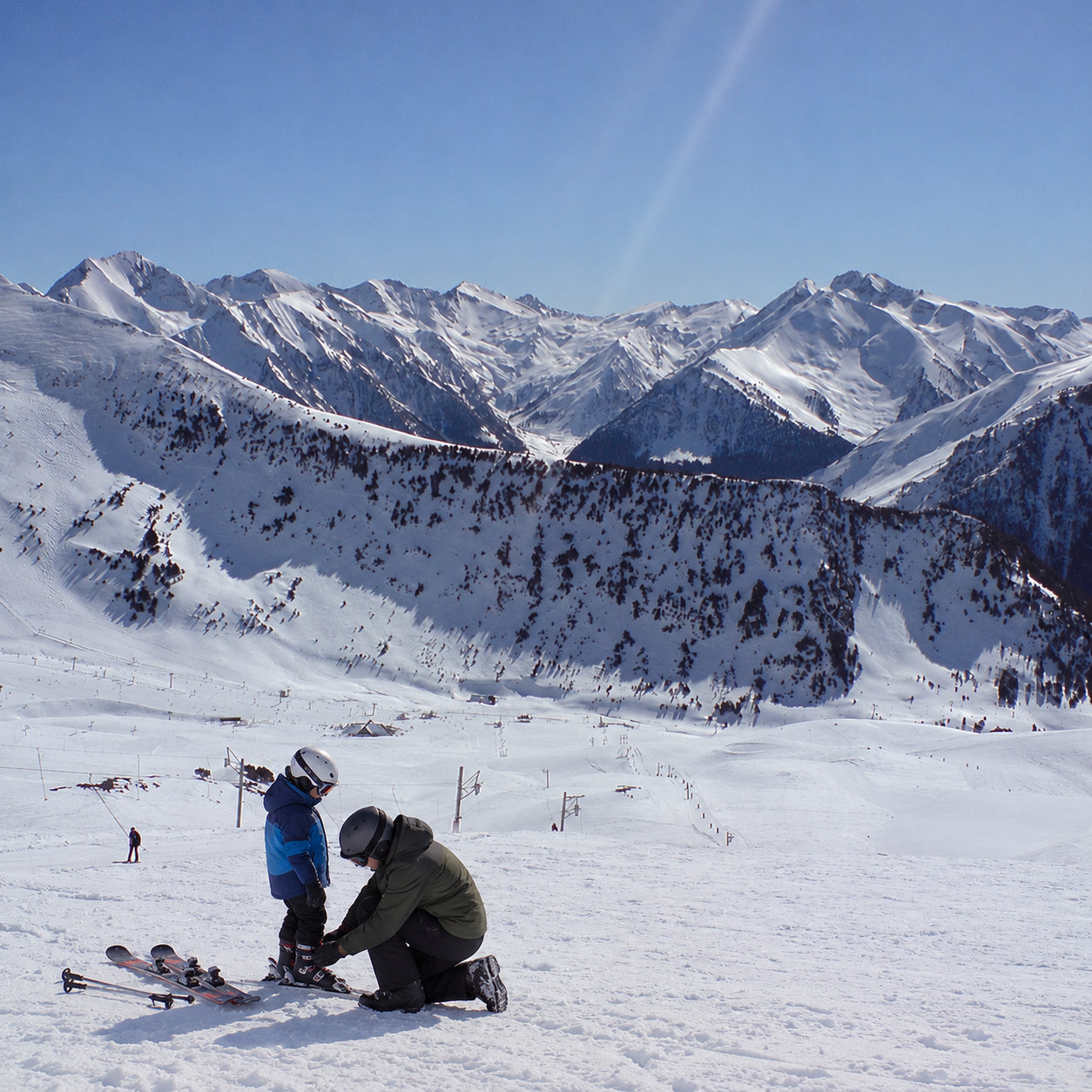 Un adulte ajuste l’équipement de ski d’un enfant sur la neige