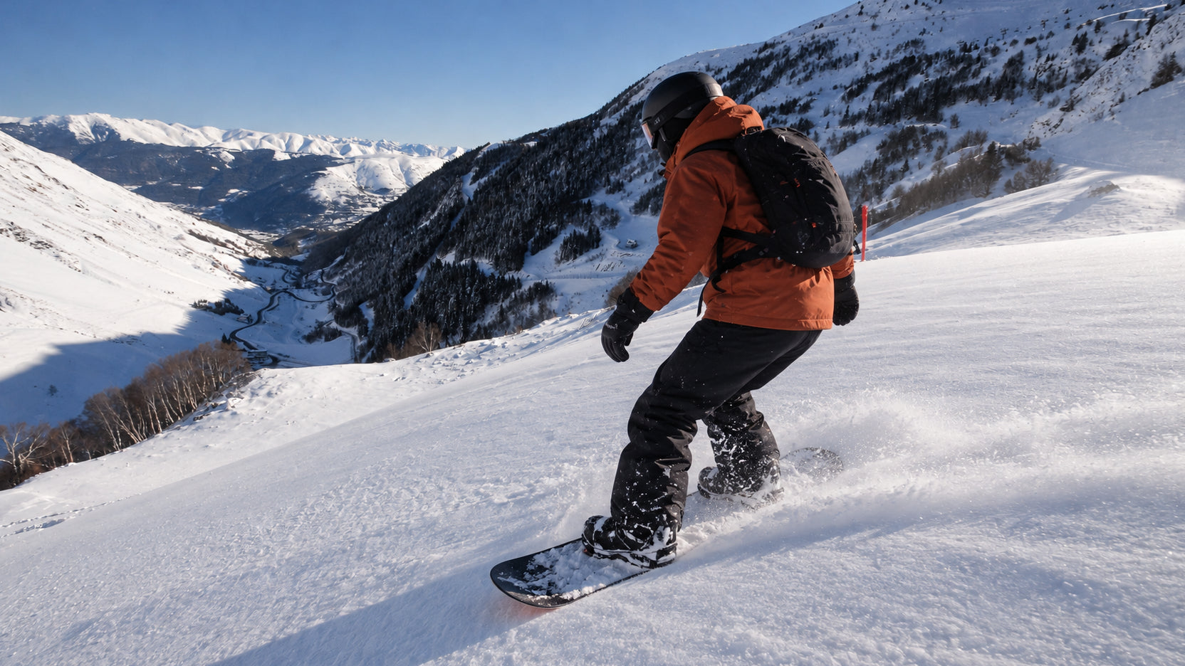 Snowboardeur en veste orange sur une piste enneigée devant des versants boisés